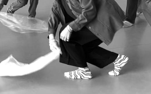 A cropped view of a dancer crouching while holding a piece of fabric.